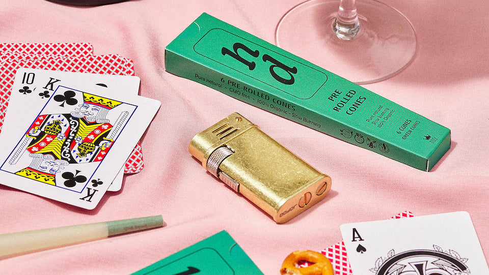 Cocktail glass with bubbles, playing cards, and a green box on a pink surface.